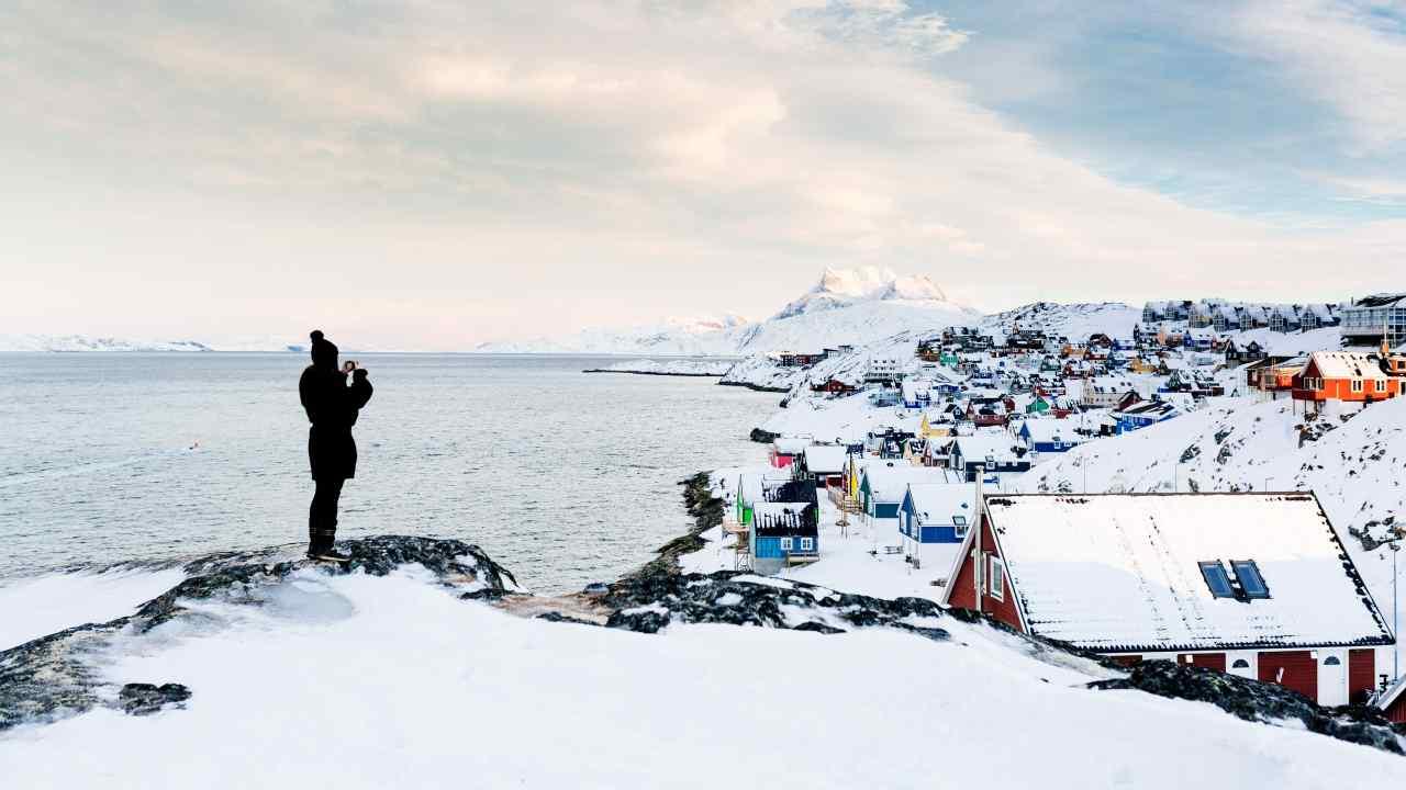 A woman stands on a ledge overlooking a town on the coast that is covered in snow