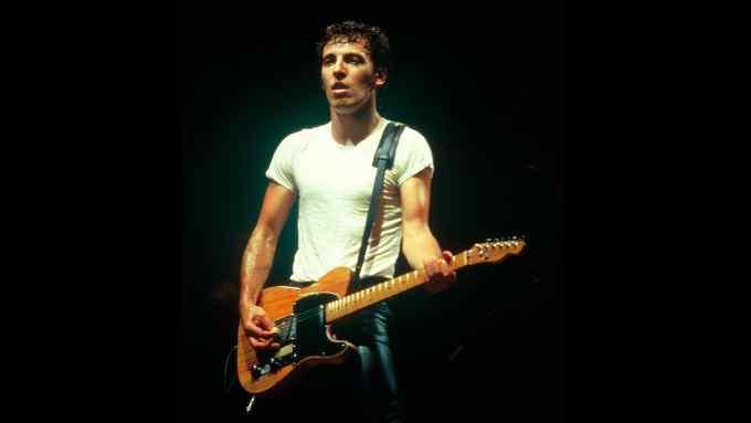 A man in white T-shirt plays a guitar on stage